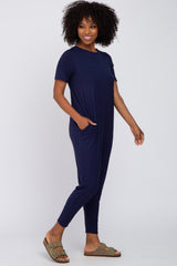 woman wearing a navy blue short sleeve jumpsuit with pockets and styled with green slide sandals