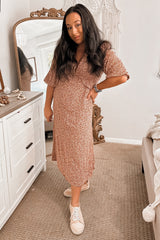 woman wearing a pink floral maternity dress and white sneakers, posing with one hand on her hip and a visible baby bump