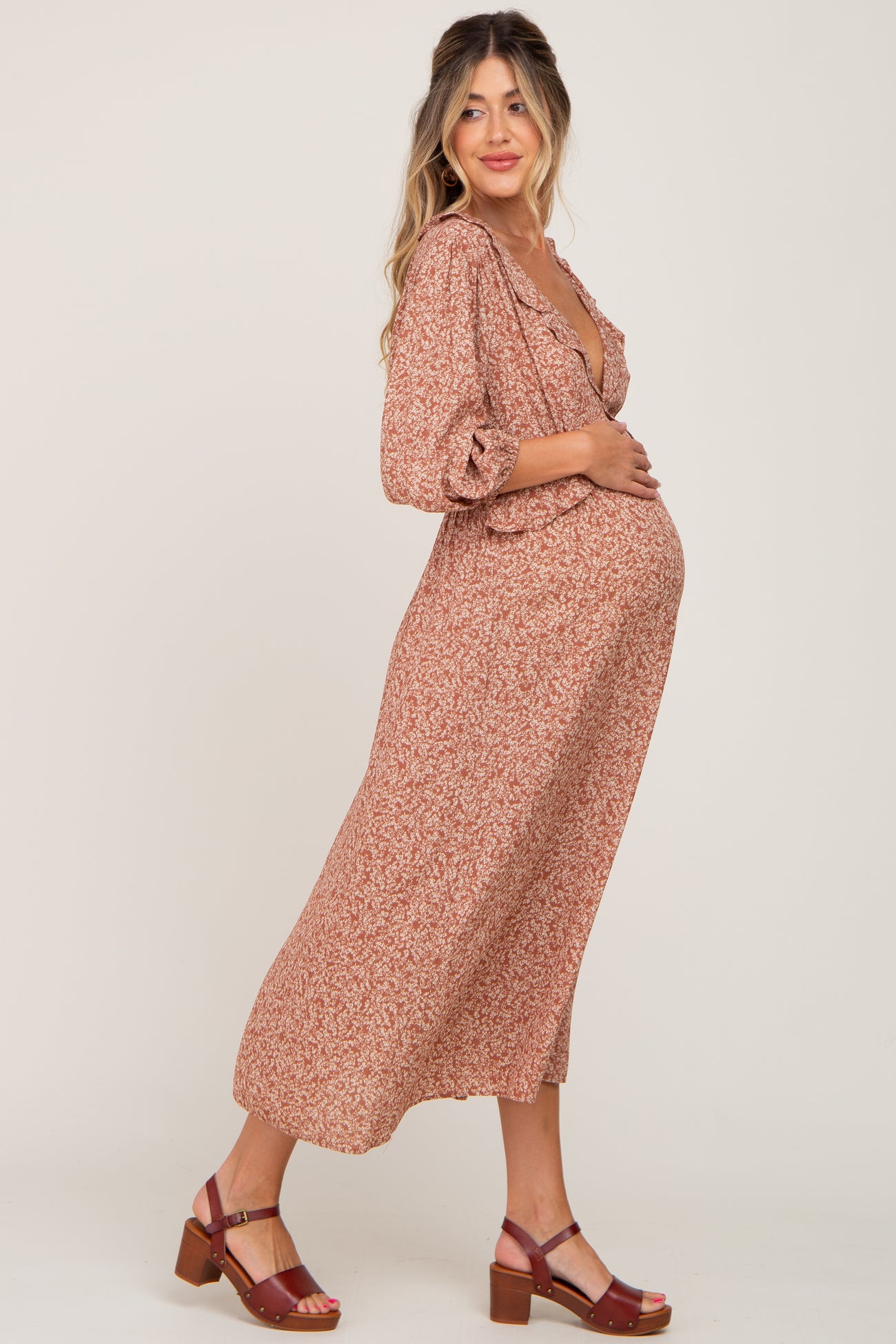 woman wearing a rust-colored floral maternity dress with a deep neckline and holding her baby bump