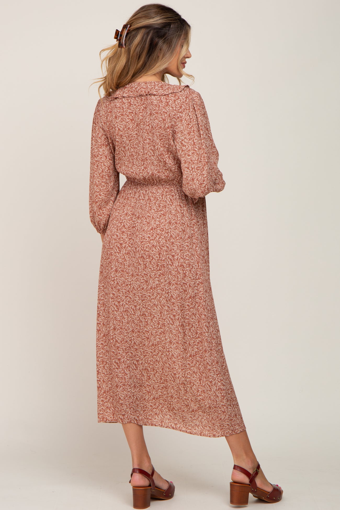 woman wearing a rust-colored floral maternity maxi dress with long sleeves and a cinched waist, showing her baby bump