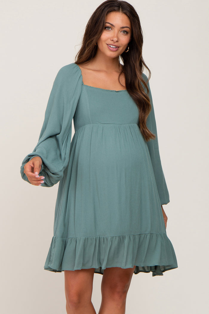 woman wearing a sage green maternity dress with balloon sleeves and a ruffled hem, showing her baby bump