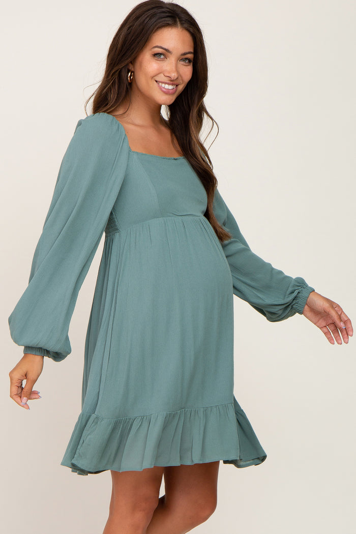 woman wearing a sage green maternity dress with long sleeves and a ruffle hem, showcasing her baby bump