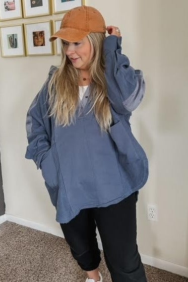 woman wearing an oversized blue quarter-zip pullover sweatshirt and an orange baseball cap