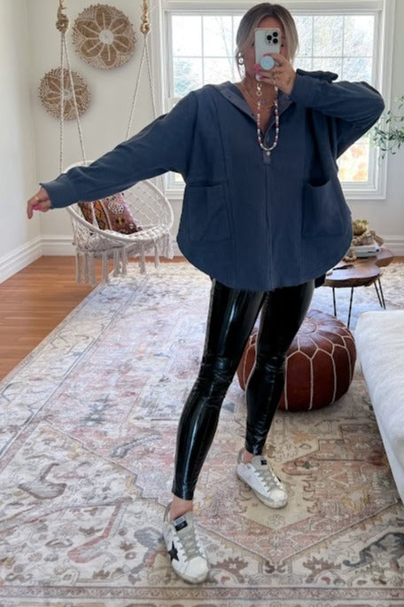 woman wearing a navy blue oversized zip-up hoodie with two front pockets and shiny black leggings, styled with sneakers