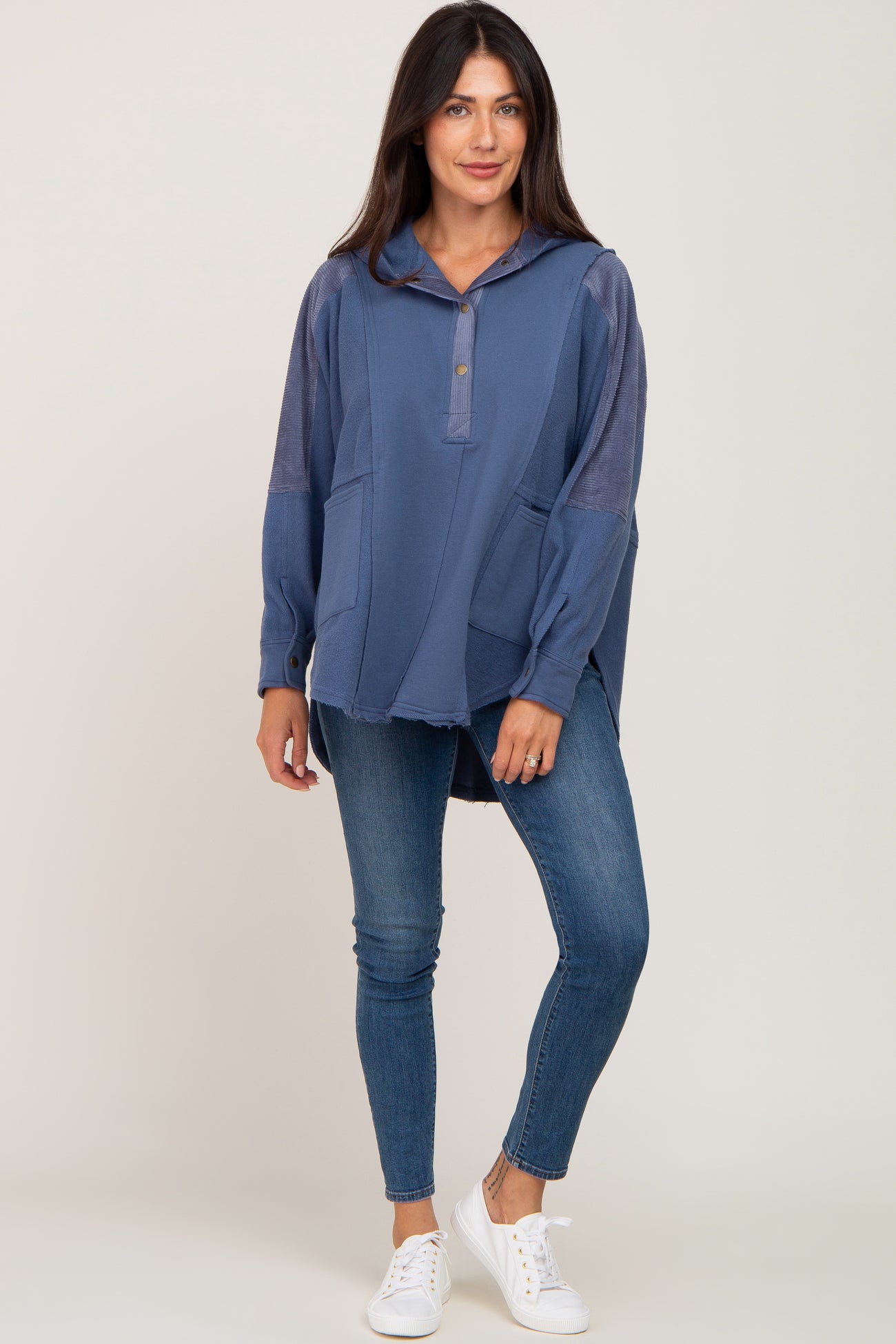 woman wearing a blue hooded pullover with two front pockets and distressed hem, paired with skinny jeans and white sneakers