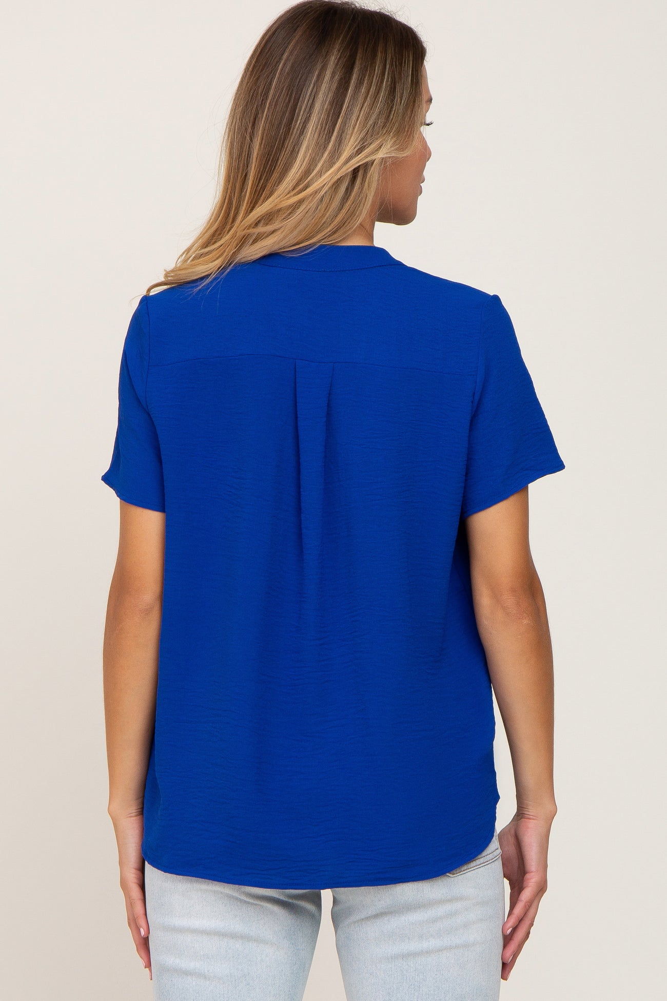 woman wearing a blue short sleeve blouse with a subtle texture and back pleat, viewed from the back
