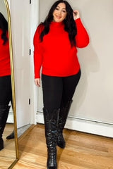 woman wearing a red maternity sweater and black leggings, standing in front of a mirror with a baby bump visible