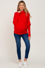 woman wearing a red maternity sweater with a cowl neck and a visible baby bump paired with blue jeans and white sneakers