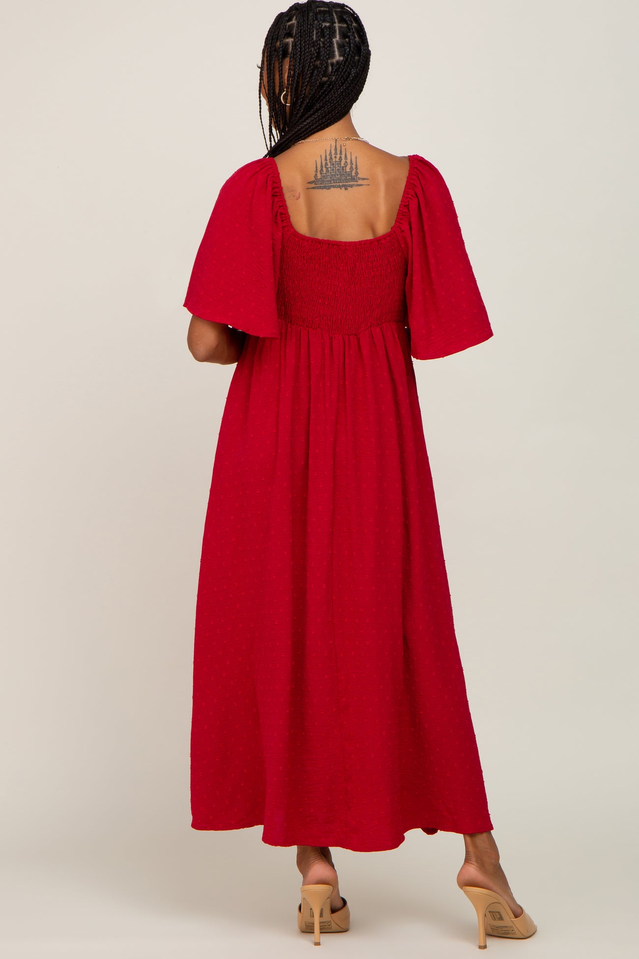 Back view of a woman wearing a red swiss dot maternity maxi dress with flutter sleeves and a smocked back.