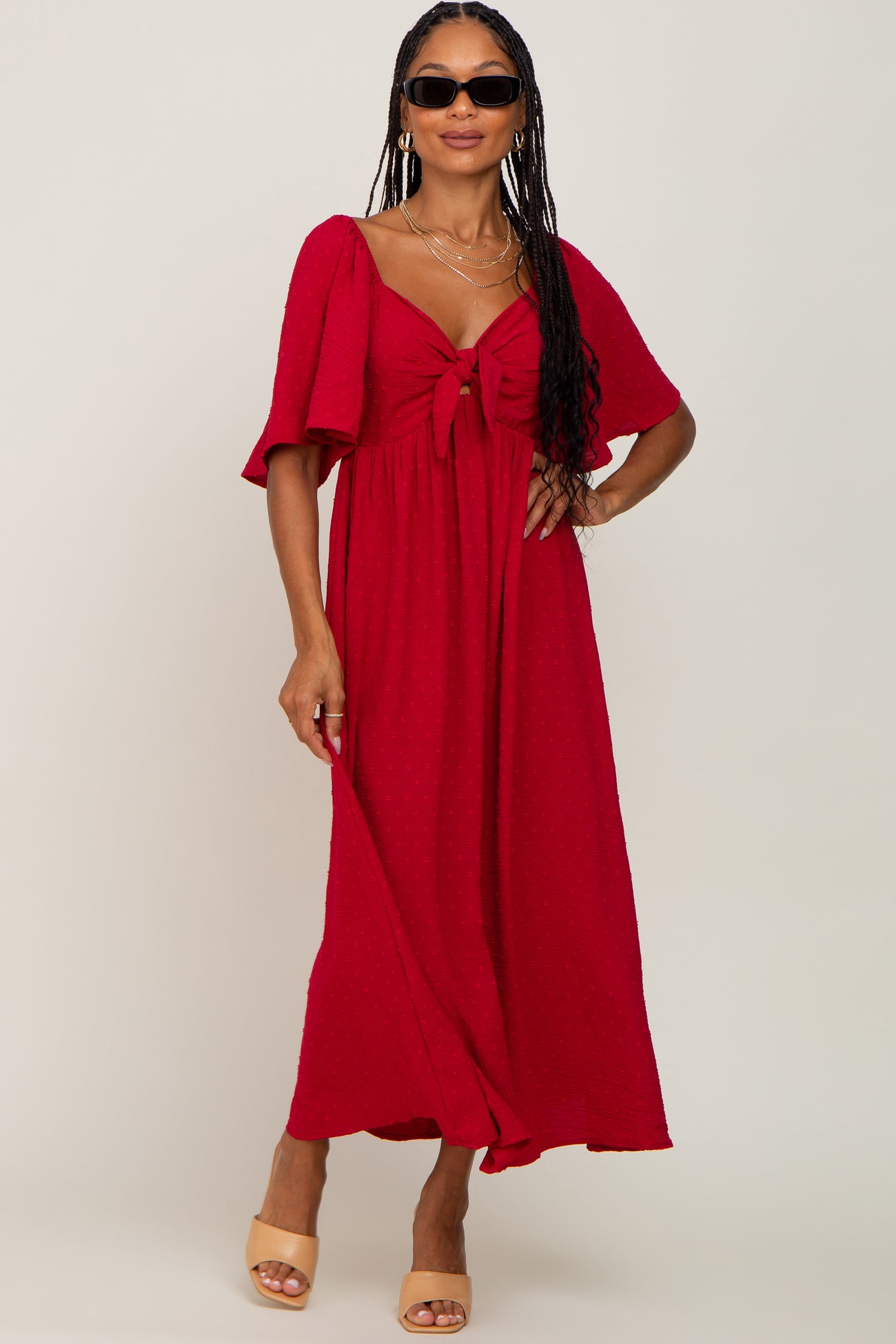 woman wearing a red maxi dress with a tie front detail and short sleeves, accessorized with sunglasses and heeled sandals