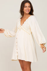 smiling pregnant woman wearing a cream maternity mini dress with lace bodice and long balloon sleeves