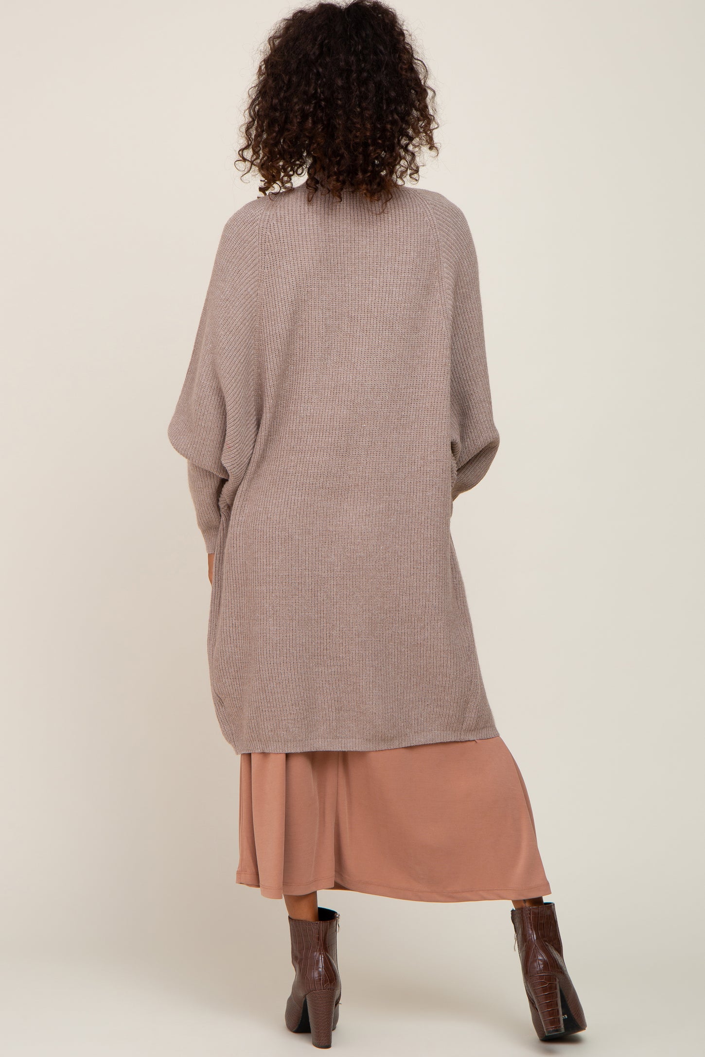 woman wearing a beige oversized knitted cardigan over a rust-colored midi dress and brown heeled ankle boots