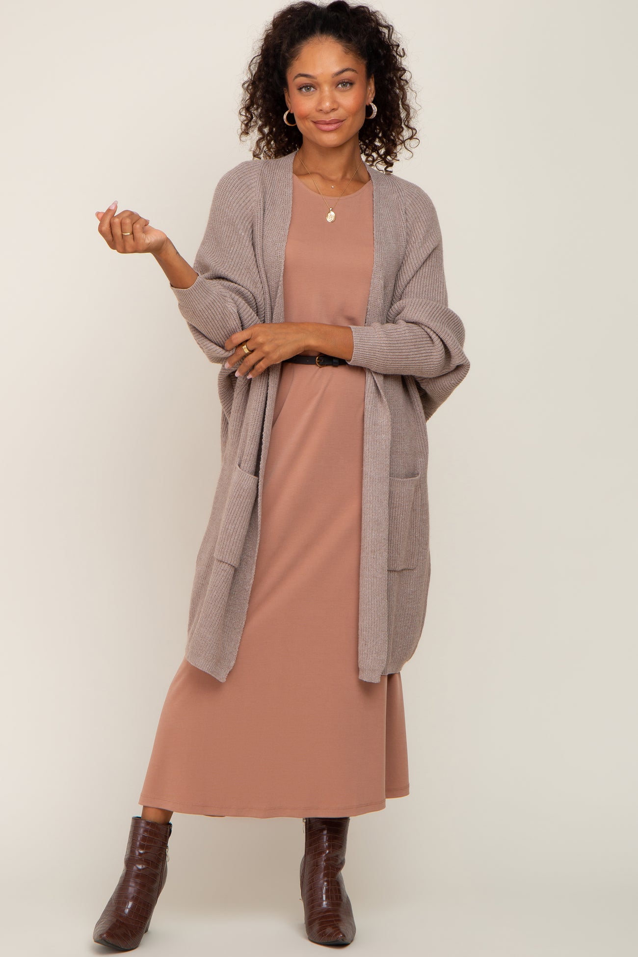 woman wearing a taupe long cardigan over a dusty rose maxi dress with curly hair and brown ankle boots