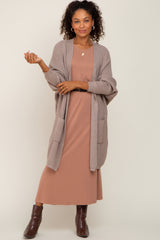 woman wearing a taupe long cardigan over a dusty rose maxi dress with curly hair and brown ankle boots