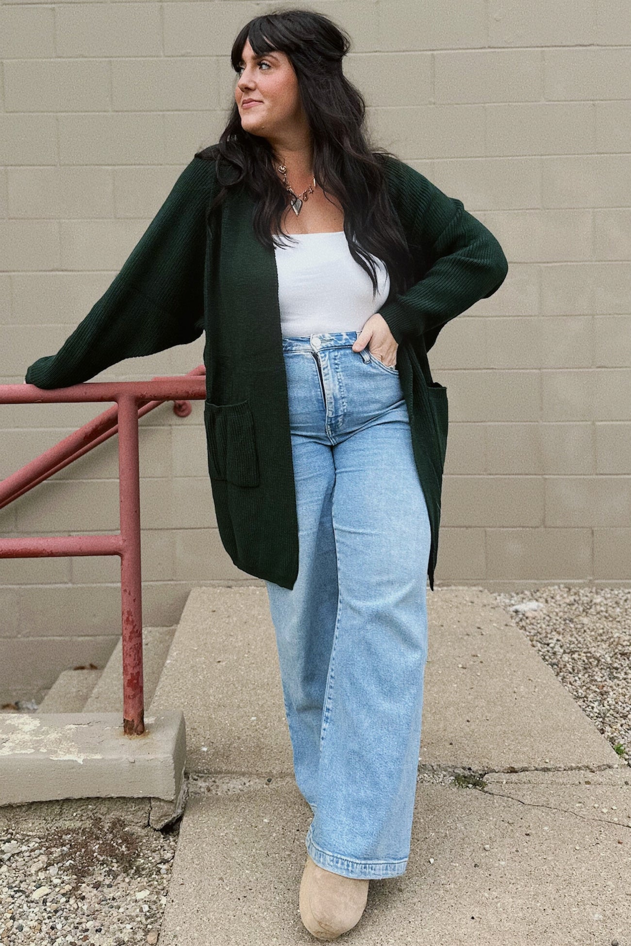 woman wearing an oversized dark green cardigan, white tank top, and light blue wide-leg jeans