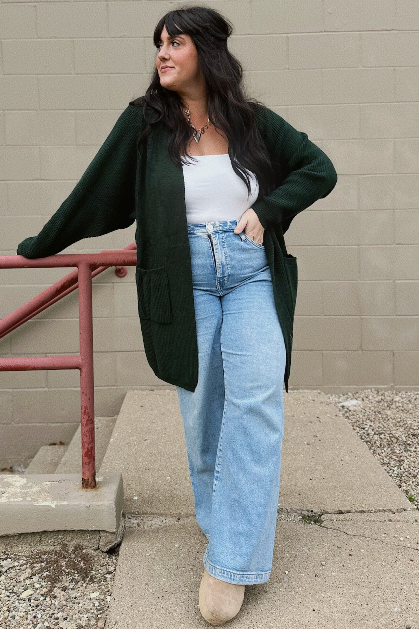 woman wearing an oversized dark green cardigan, white tank top, and light blue wide-leg jeans