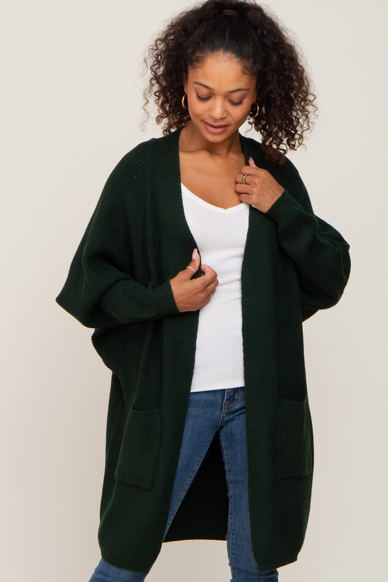 woman wearing a dark green oversized cardigan with pockets, paired with a white top and blue jeans