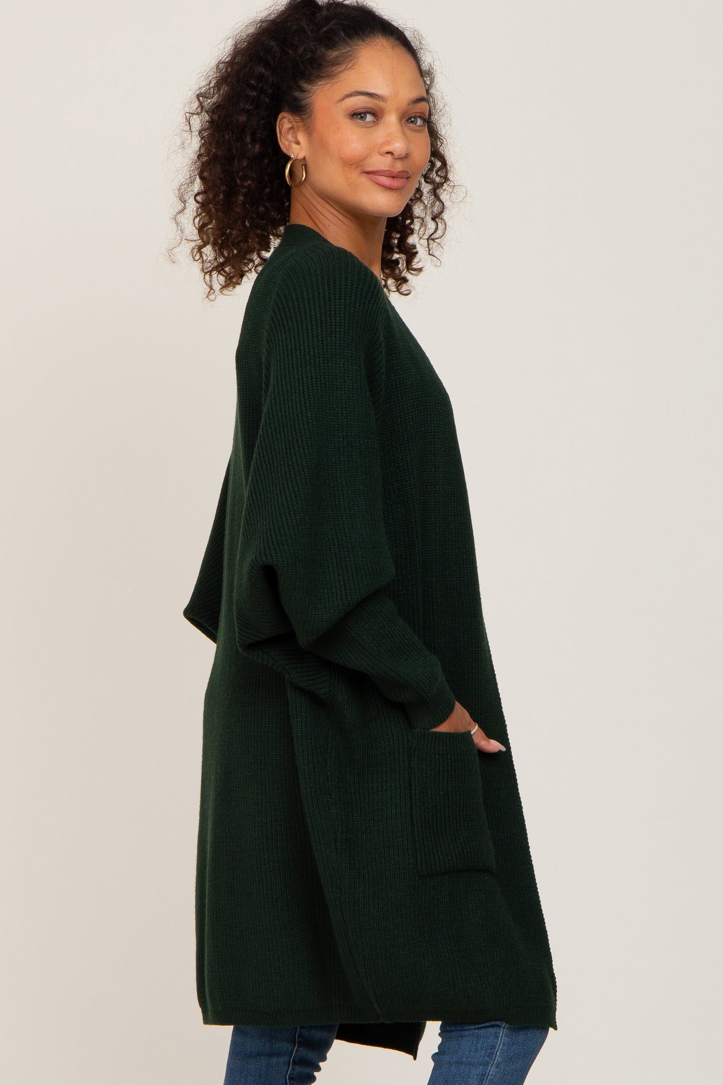 woman wearing a dark green oversized cardigan with pockets and a relaxed fit, styled with blue jeans