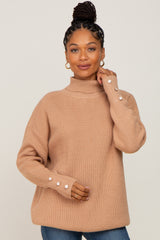 woman wearing a beige turtleneck sweater with ribbed texture and button details on the sleeves