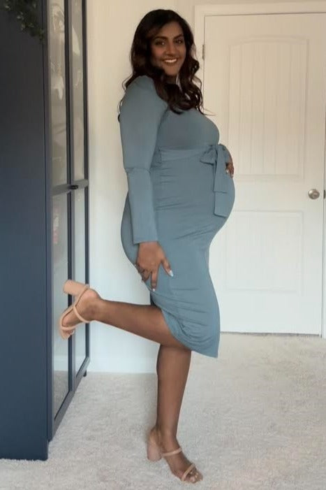 pregnant woman in a long-sleeved blue maternity dress and tan heels posing in a room