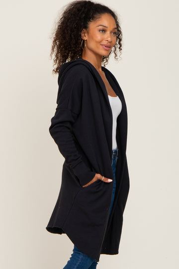 woman wearing a black long hooded cardigan with pockets, styled over a white tank top and blue jeans