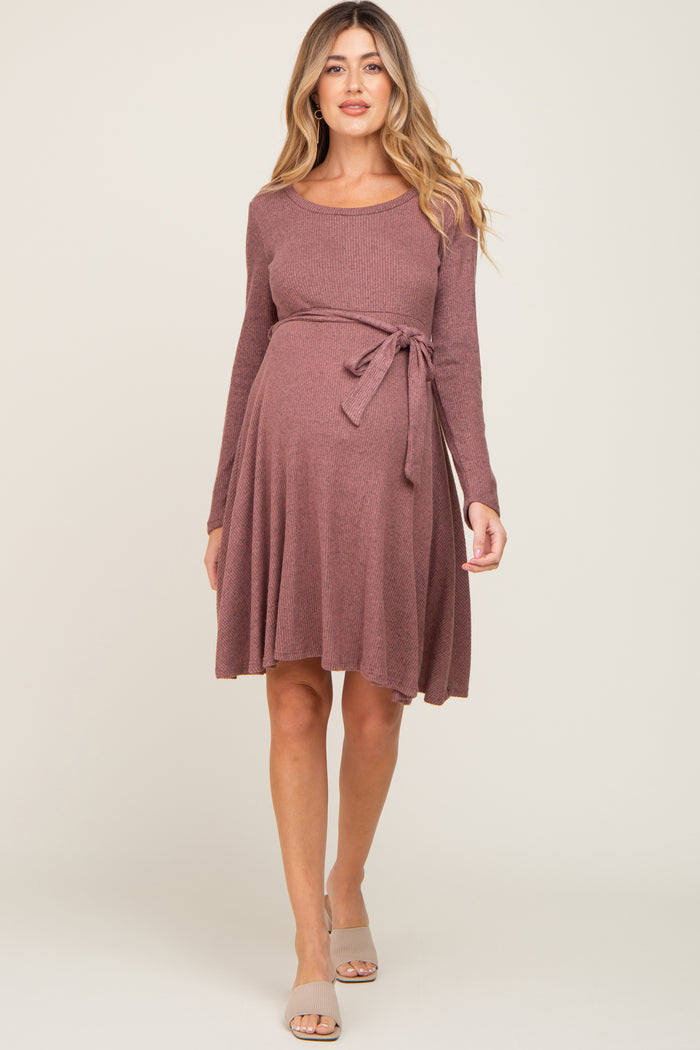 woman wearing a mauve long sleeve maternity dress with a tie waist and flared skirt, showcasing her baby bump