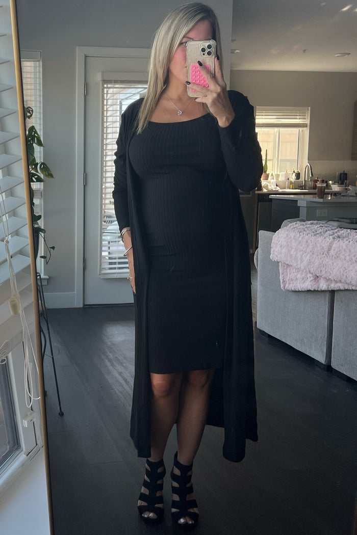 woman wearing a black maternity bodycon dress with a long black cardigan and black strappy heels, baby bump visible