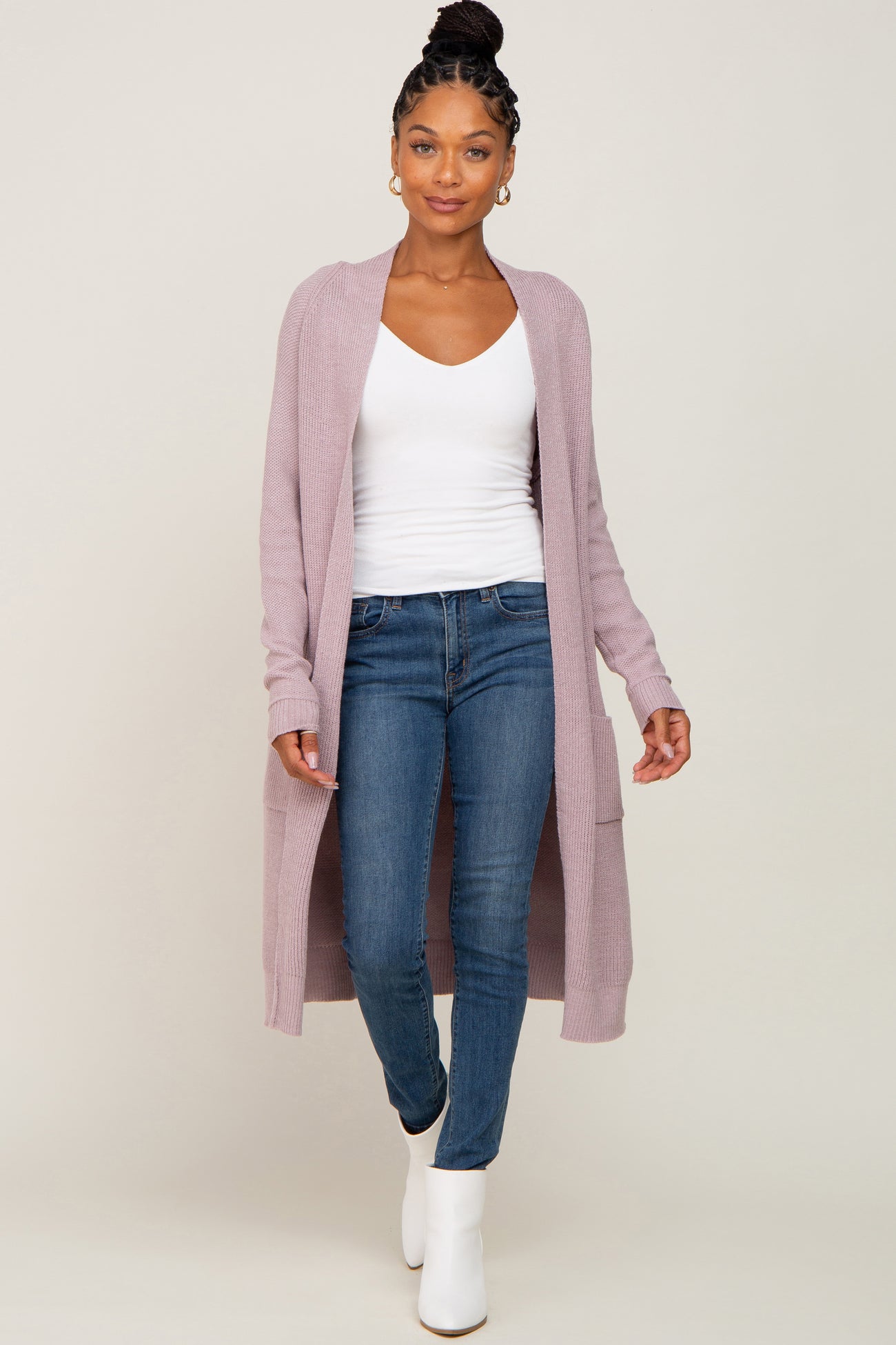 woman wearing a light purple long cardigan over a white top and blue jeans, walking in white ankle boots