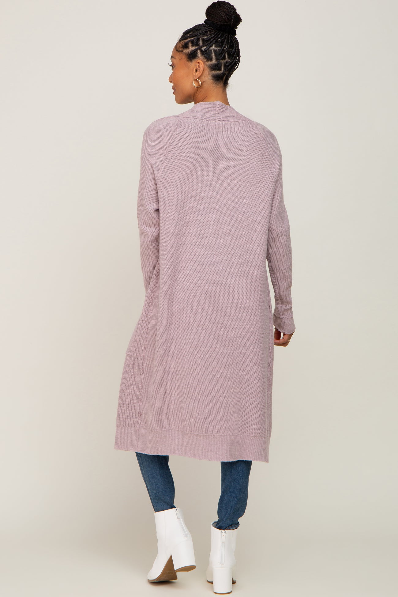 woman wearing a long lavender cardigan over jeans and white ankle boots, viewed from the back