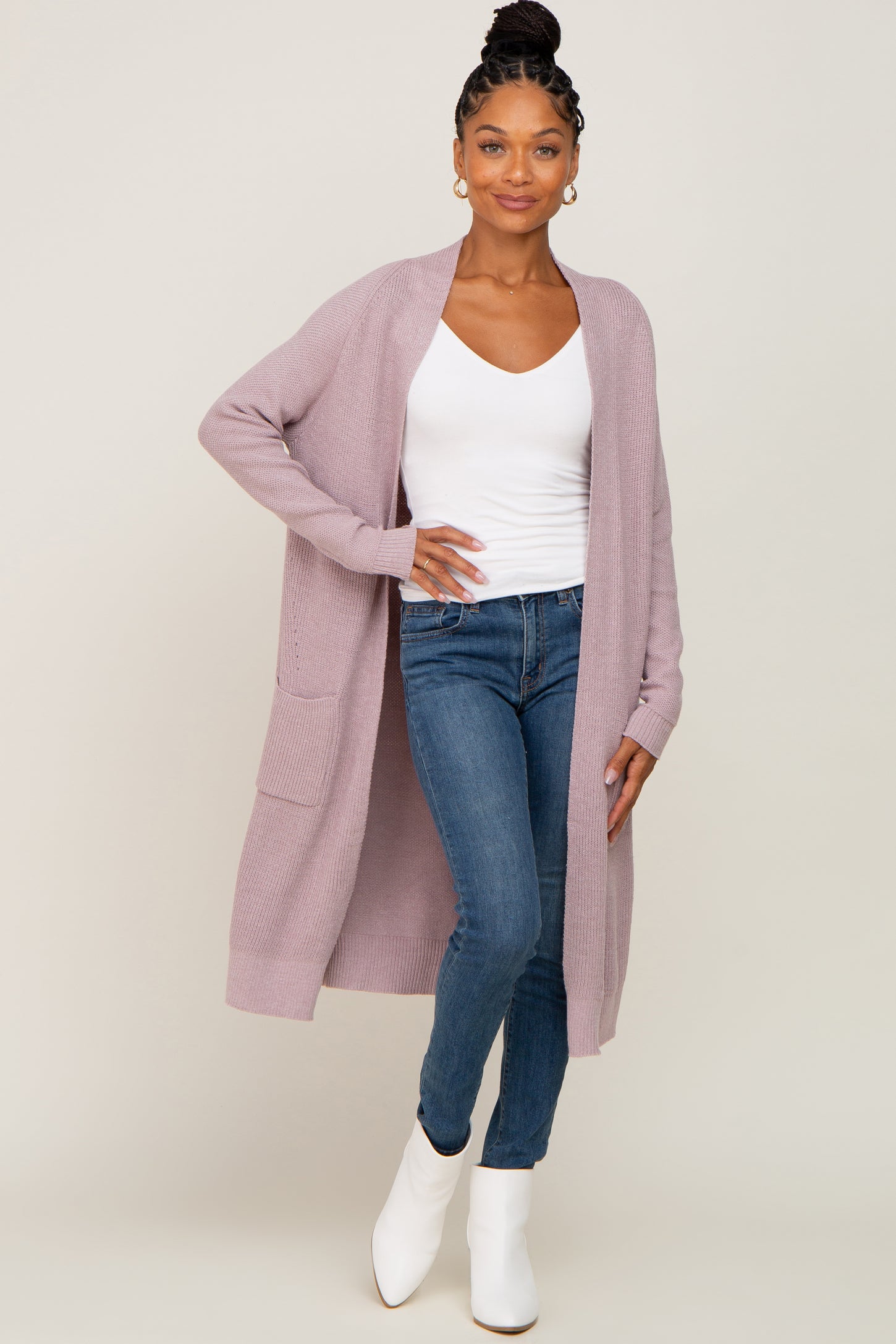 woman wearing a light purple long cardigan over a white v-neck top and blue jeans with white ankle boots