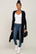 woman wearing a black long cardigan over a white v-neck top with skinny jeans and white ankle boots, holding a black clutch