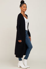 woman wearing a black long cardigan over a white top and blue skinny jeans, paired with white ankle boots