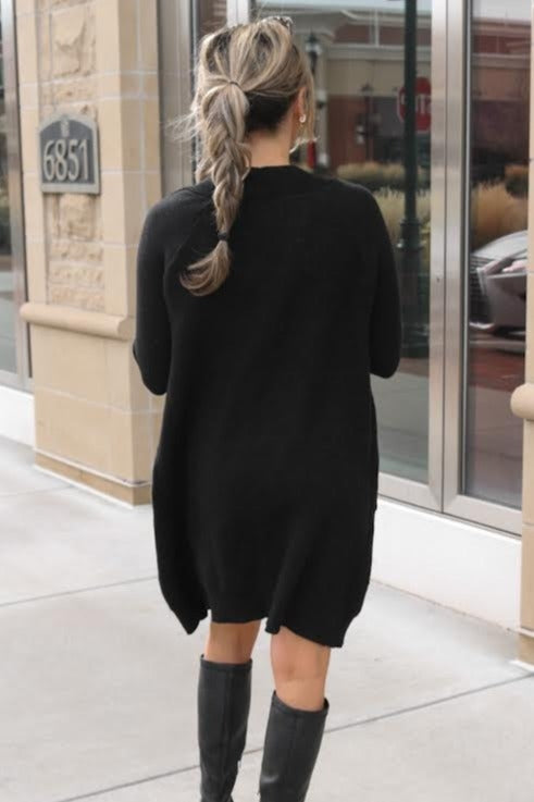woman from behind wearing a long black cardigan sweater and black knee high boots on a sidewalk