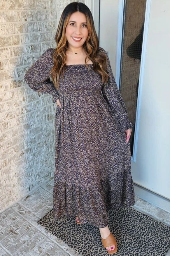 woman wearing a brown floral long sleeve maxi dress with a tiered skirt and standing by a doorway