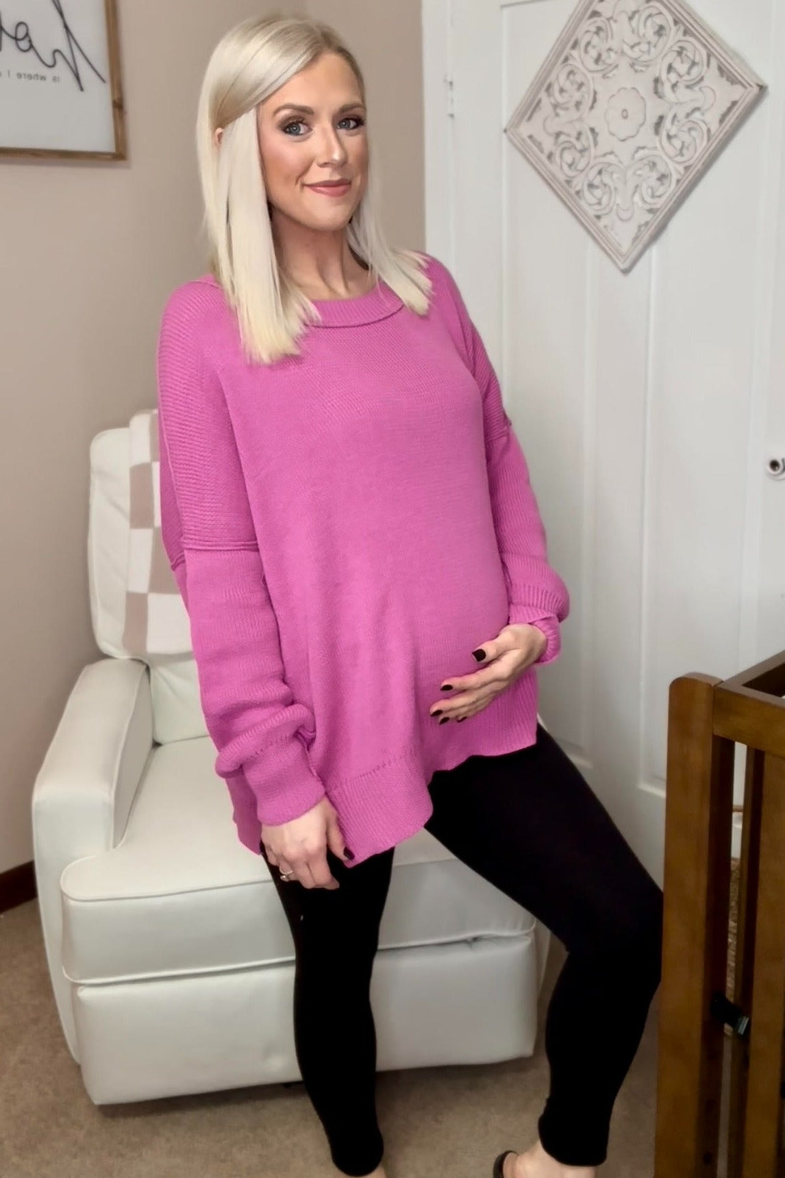 pregnant woman with blonde hair wearing a pink oversized sweater and black leggings in a nursery