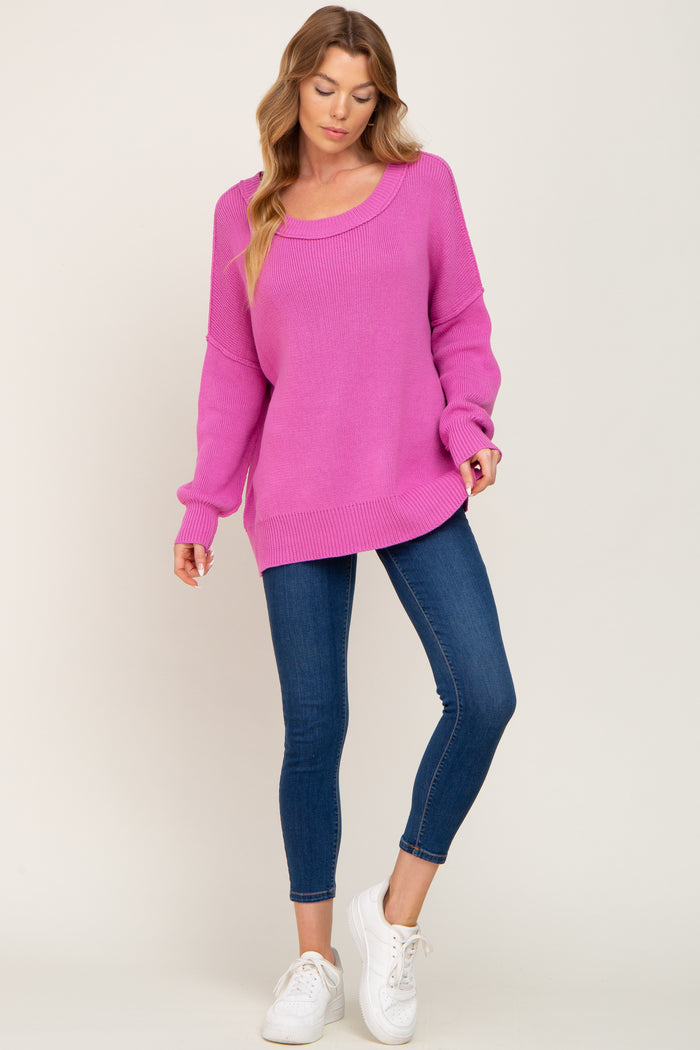 woman wearing a bright pink oversized sweater with a scoop neckline and blue skinny jeans, paired with white sneakers