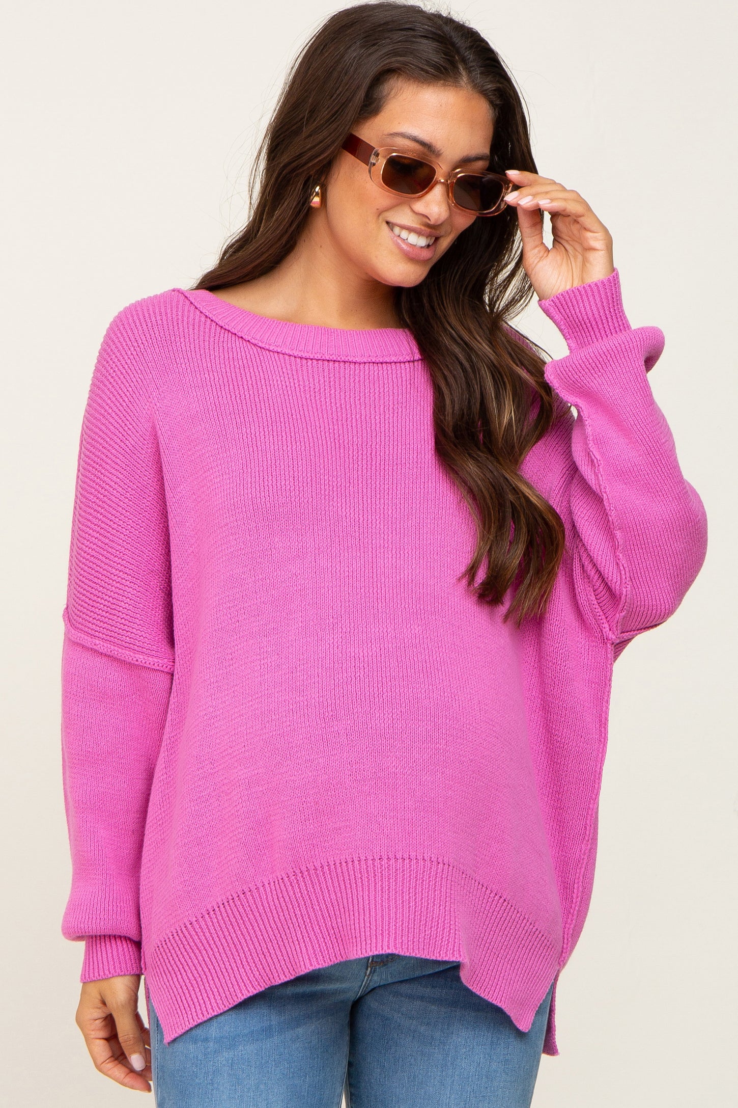 woman wearing a bright pink oversized maternity sweater with a wide neckline and long sleeves, smiling while adjusting her sunglasses