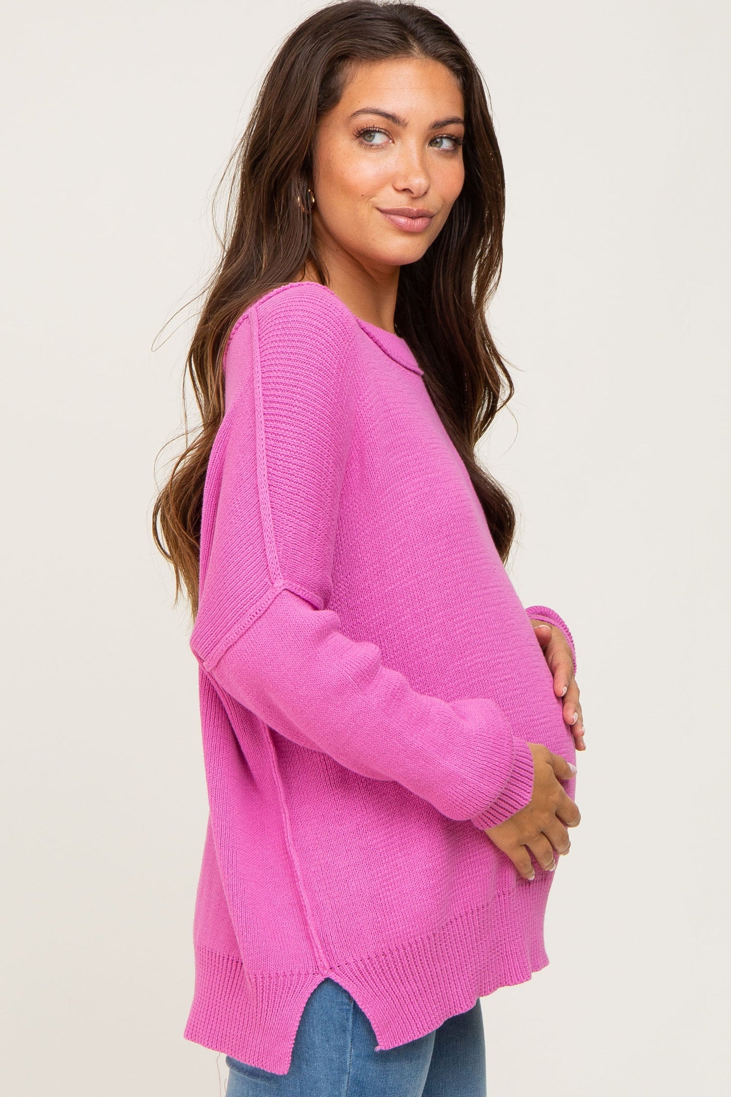 woman wearing a bright pink oversized maternity sweater and holding her baby bump