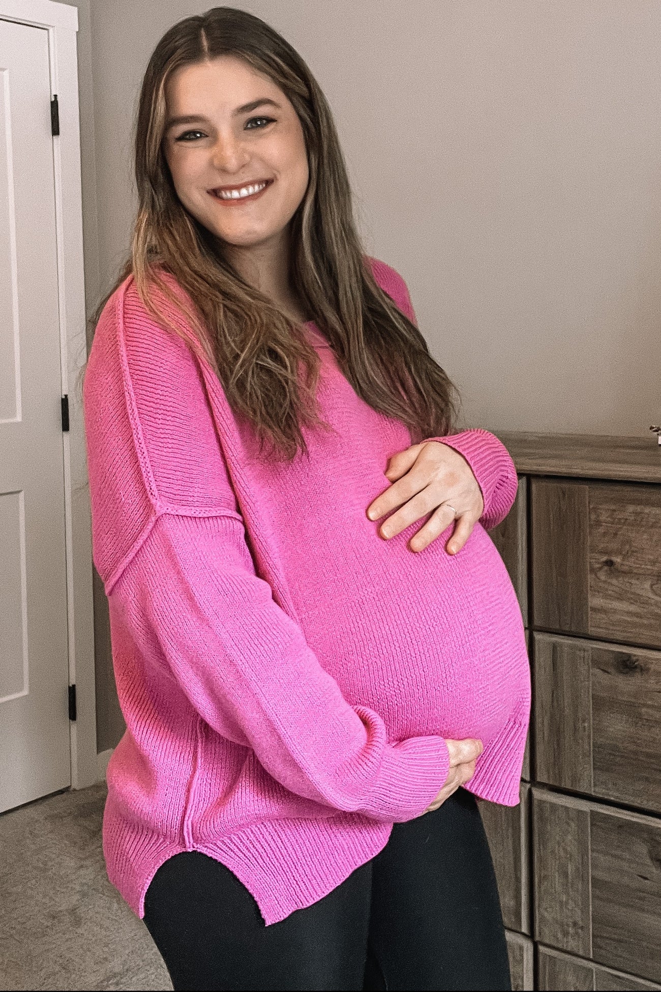 woman wearing a hot pink oversized maternity sweater and holding her baby bump