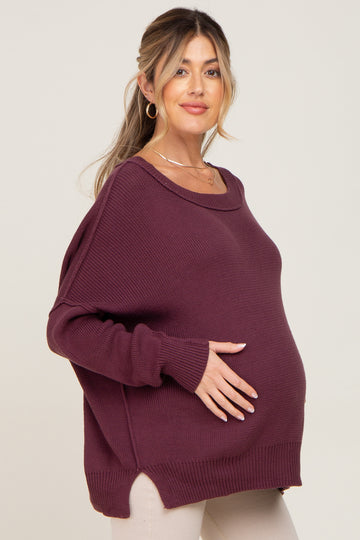 woman wearing a maroon maternity sweater with a relaxed fit and side slits, showcasing her baby bump