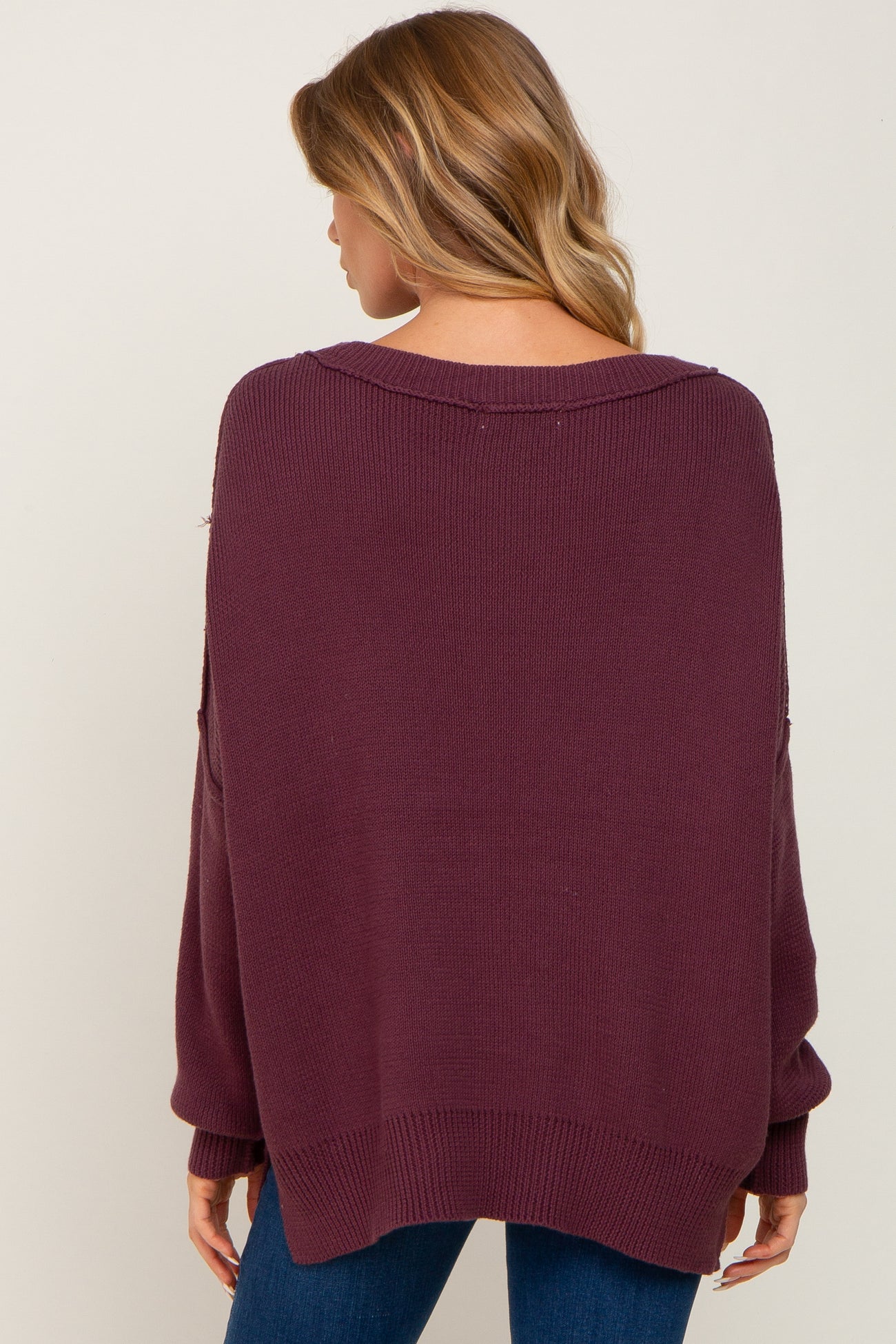 woman wearing a burgundy oversized knit sweater with a scoop neck and loose sleeves, seen from the back