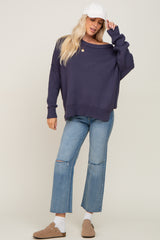 woman wearing a navy oversized sweater with off-the-shoulder detail, paired with light blue ripped straight-leg jeans and a white cap