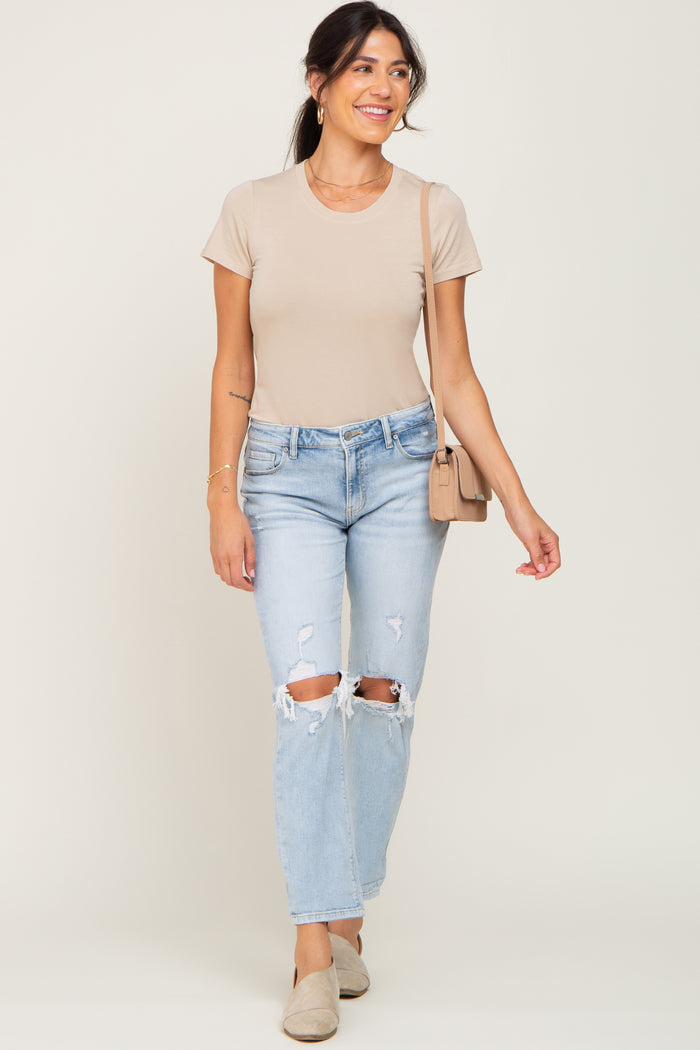 woman wearing a light beige fitted t-shirt and distressed light blue jeans, carrying a small handbag and wearing slip-on shoes