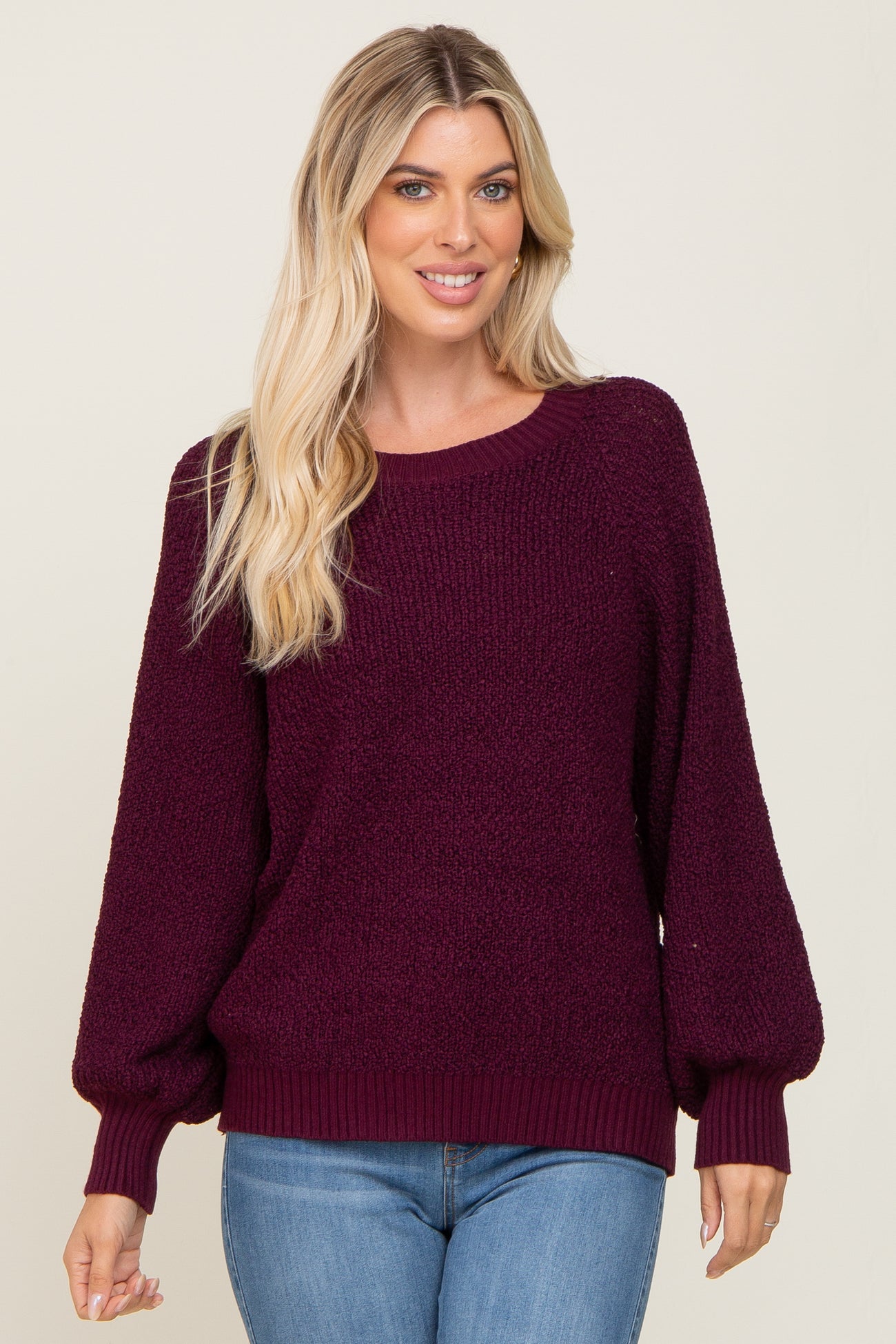 woman wearing a maroon oversized sweater with balloon sleeves and a scooped neckline, paired with blue jeans