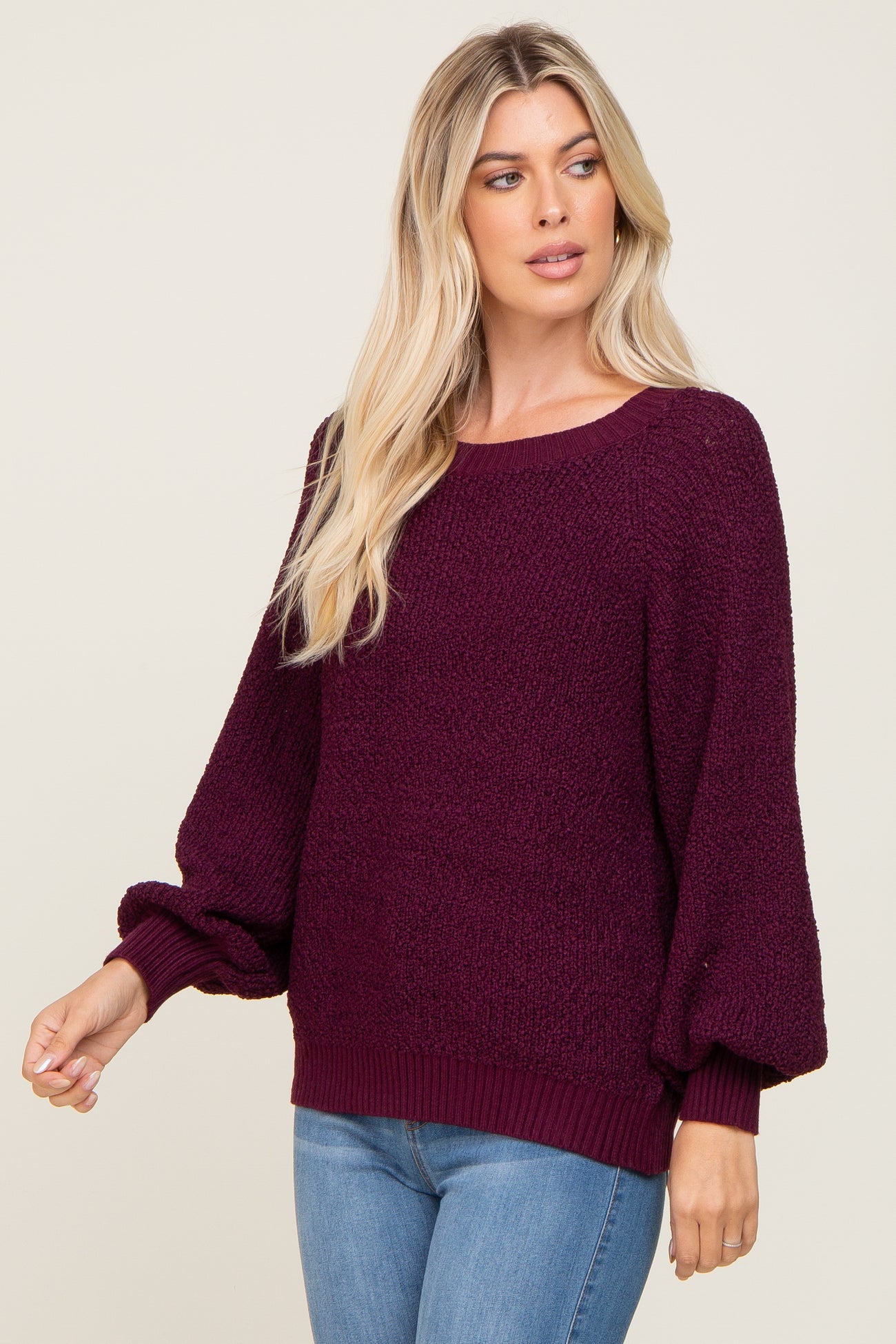 woman wearing a burgundy textured knit sweater with balloon sleeves and styled with blue jeans