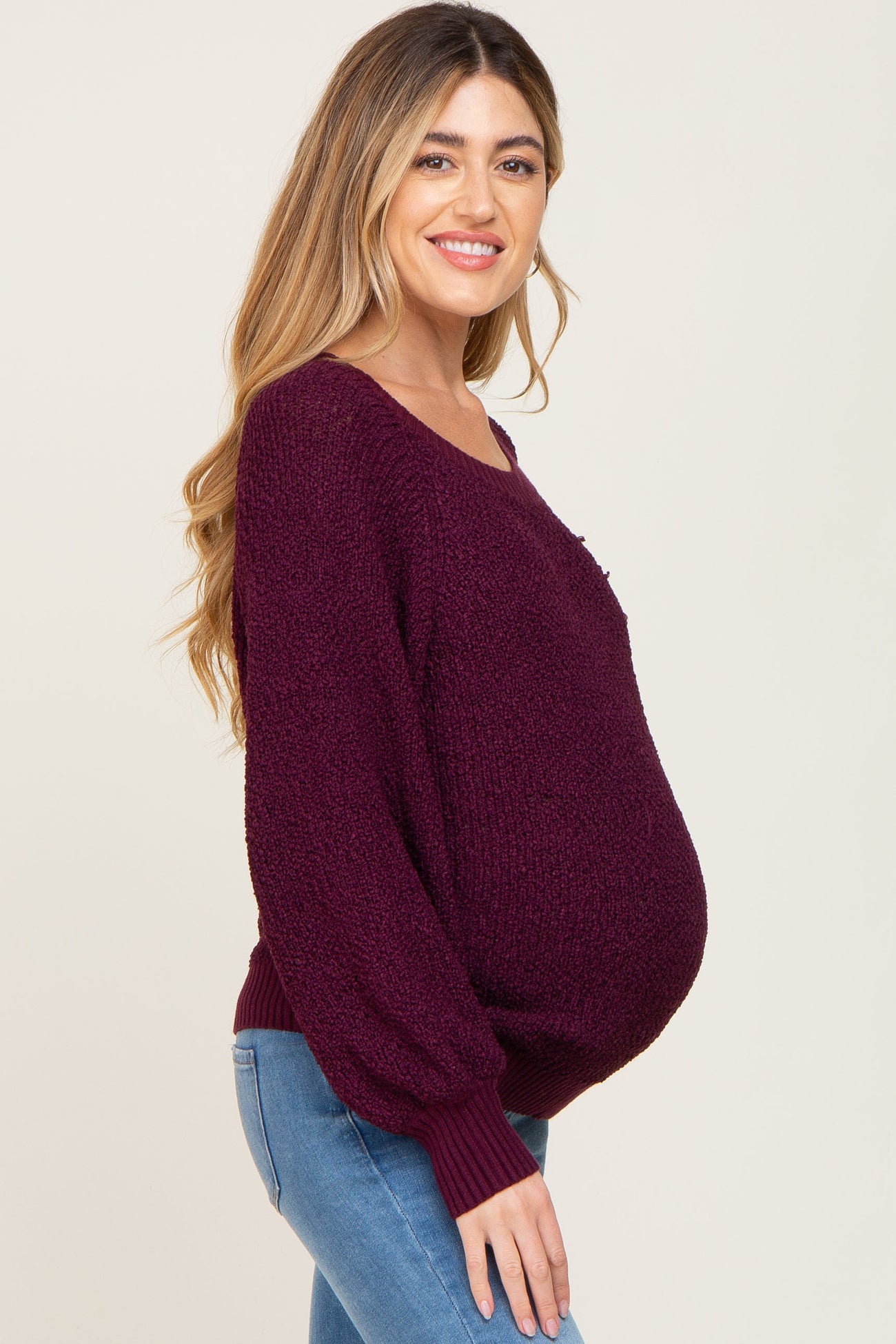 woman wearing a burgundy maternity sweater with a relaxed fit and balloon sleeves, showcasing her baby bump