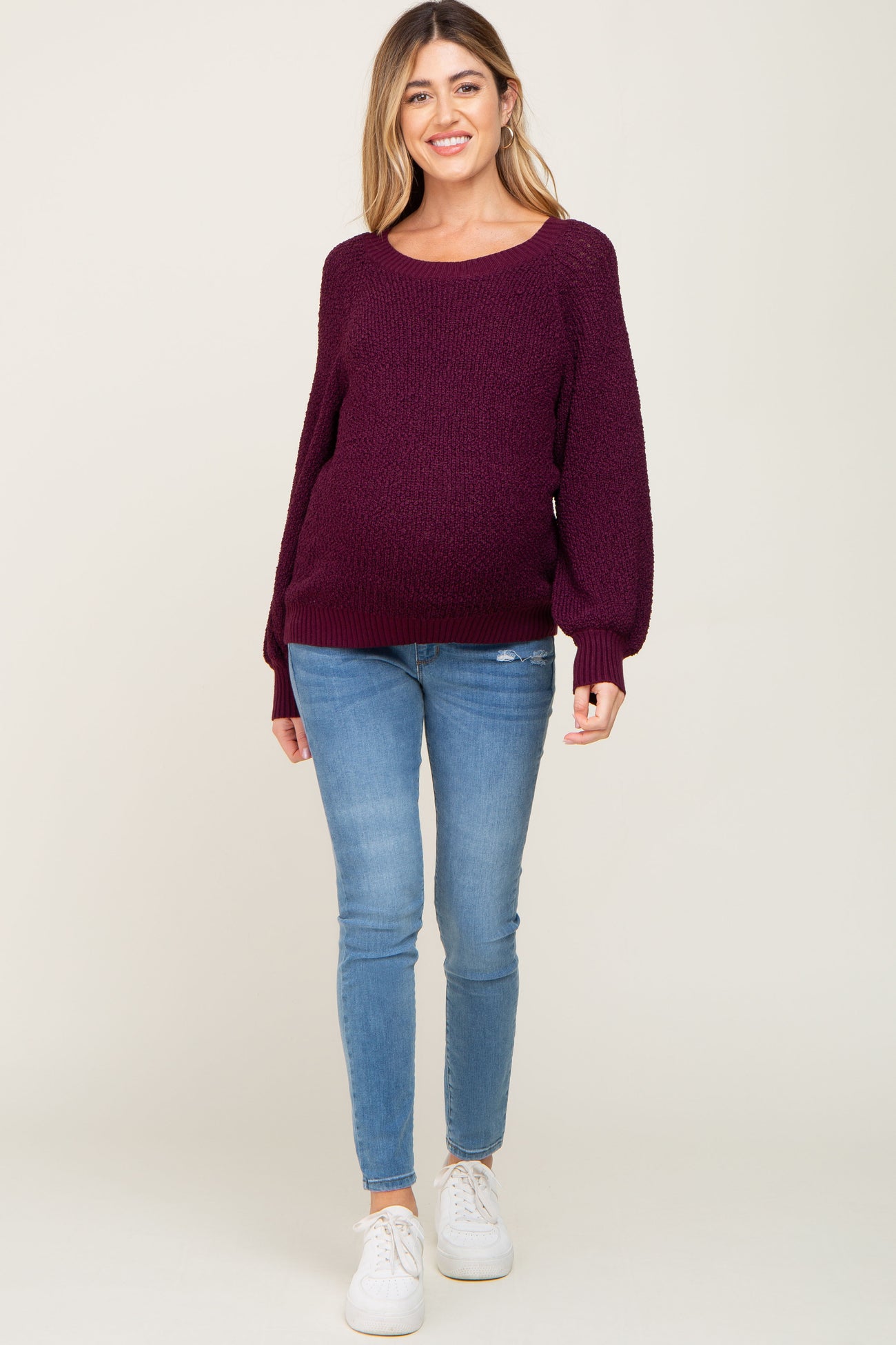 woman wearing a burgundy oversized maternity sweater and blue skinny jeans, showing her baby bump
