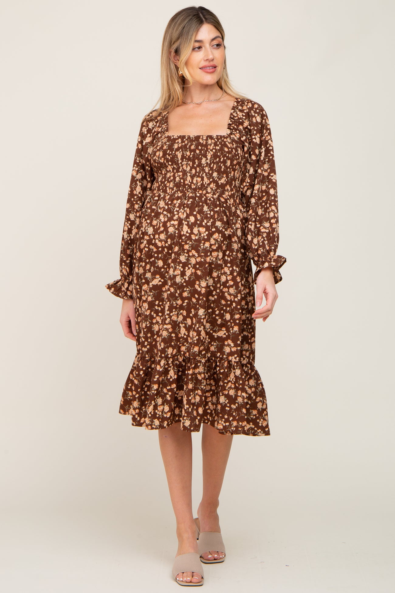 woman wearing a brown floral maternity dress with a square neckline and ruffled hem, showcasing her baby bump