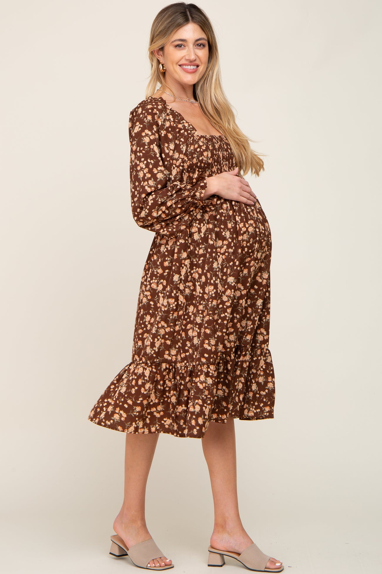 Pregnant woman in a brown floral long sleeve maternity midi dress with smocked bodice and ruffled hem