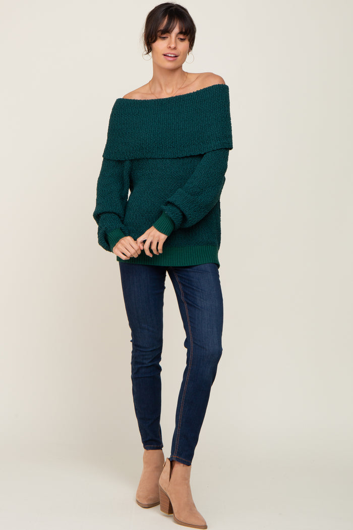 woman wearing a dark green off-the-shoulder knit sweater with dark blue skinny jeans and tan ankle boots